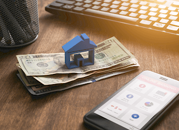 small blue plastic model of a house on top of a stack of cash